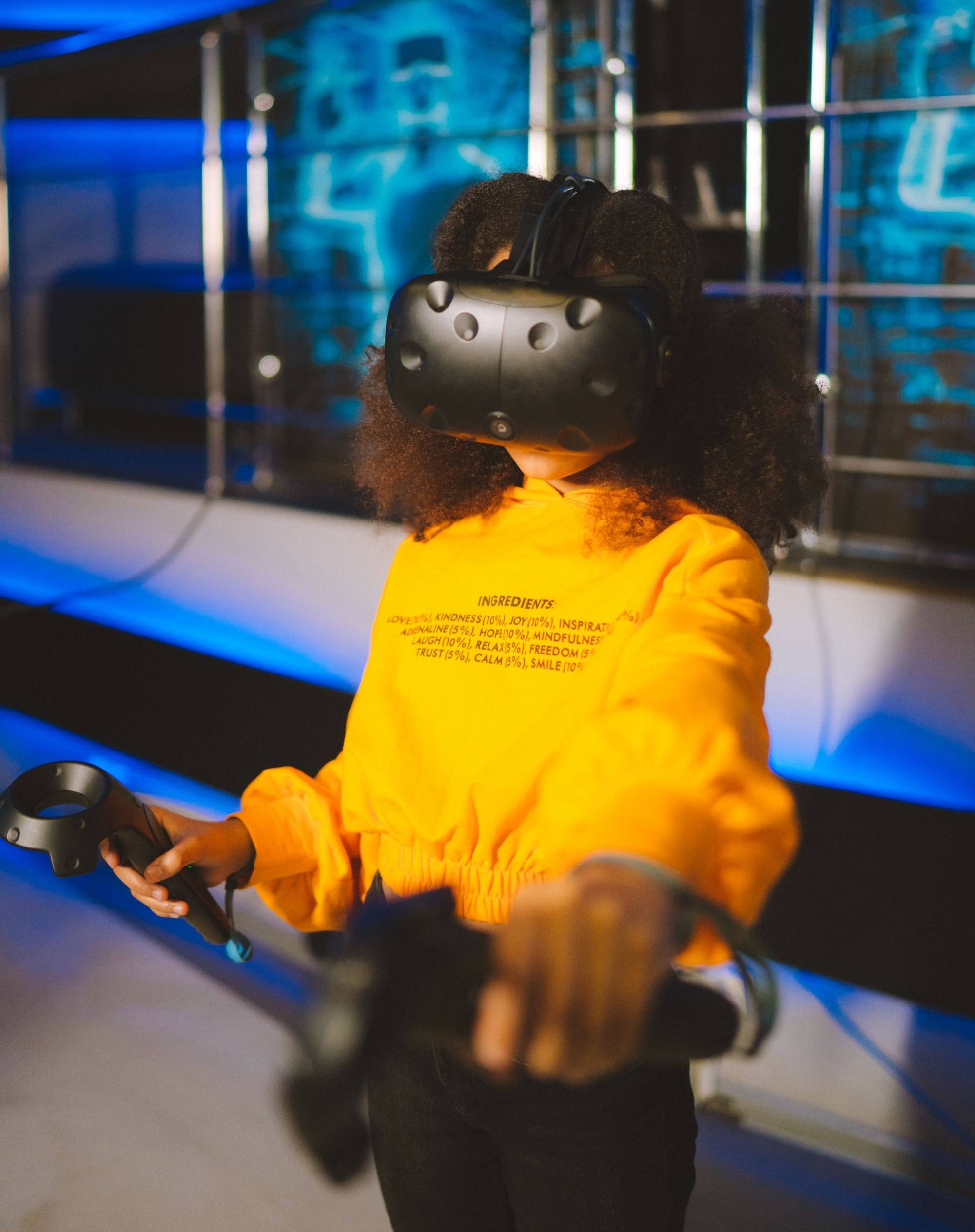 A girl wearing a virtual reality headset reaches forward with hand controllers.