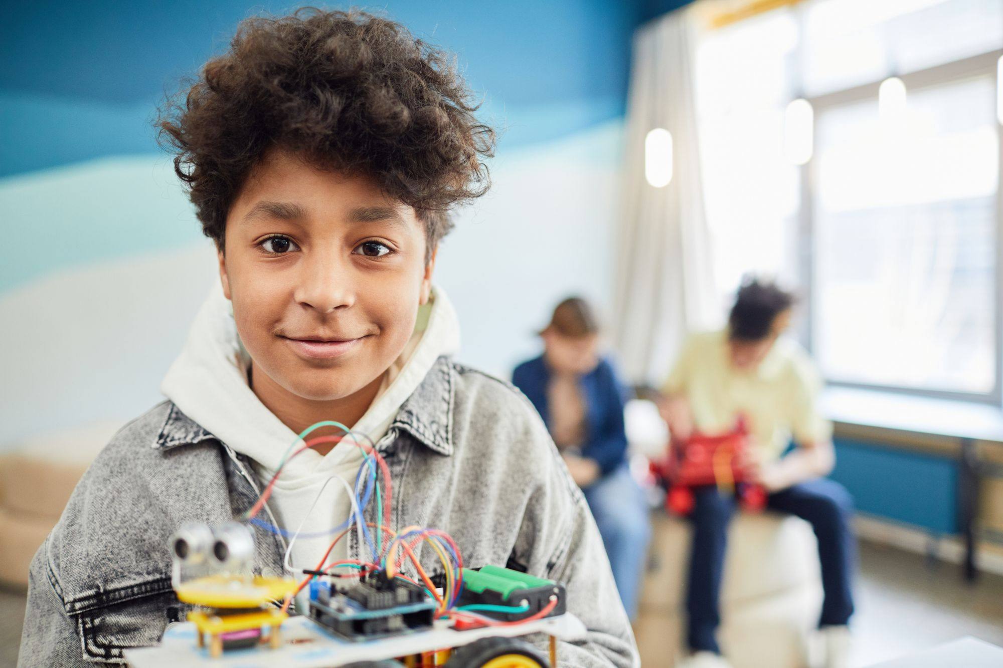 A smiling boy sits behind an electronics project with wires and a circuit board.