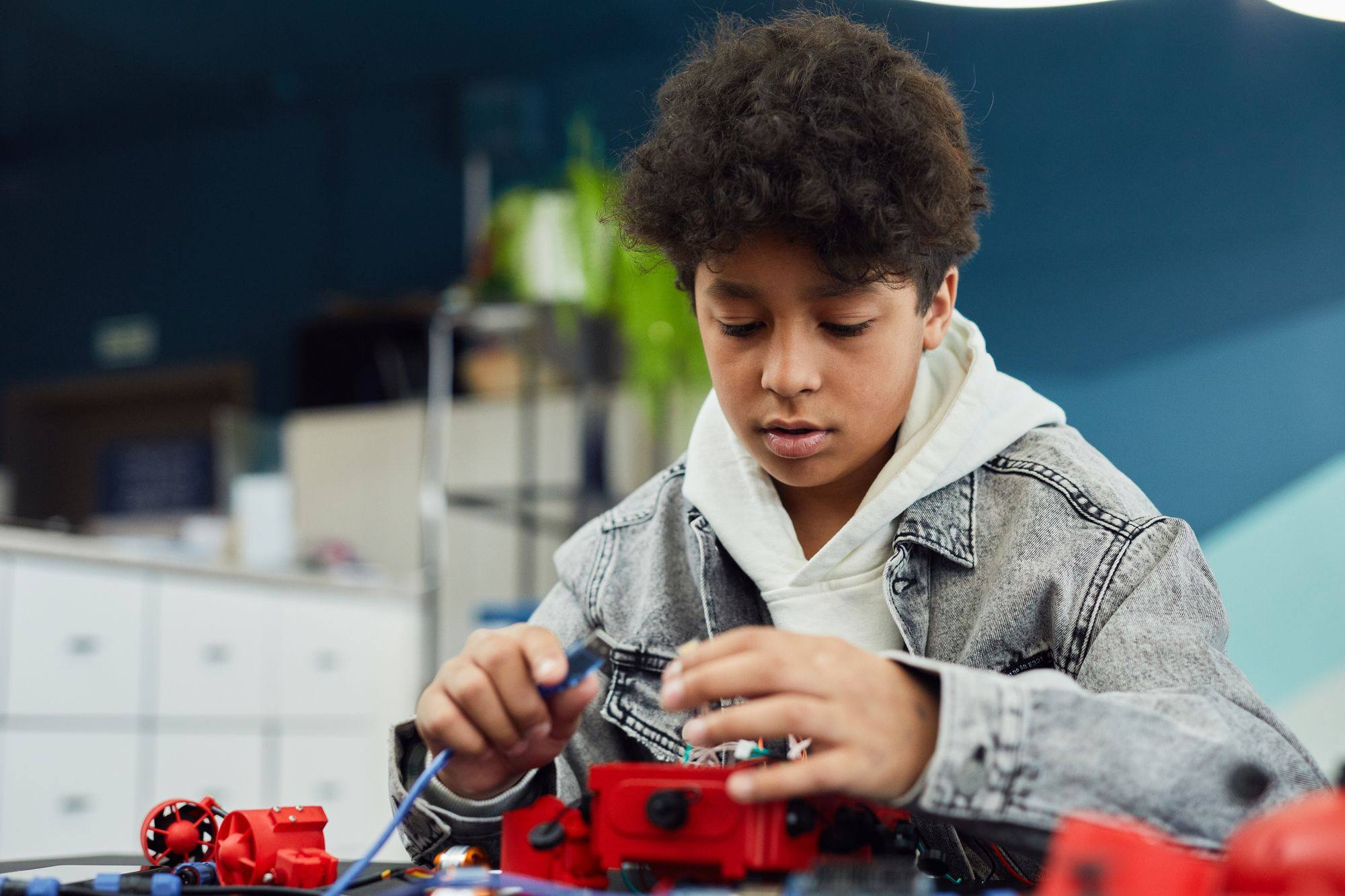 A boy in a denim jacket concentrates as he wires a robotics project.