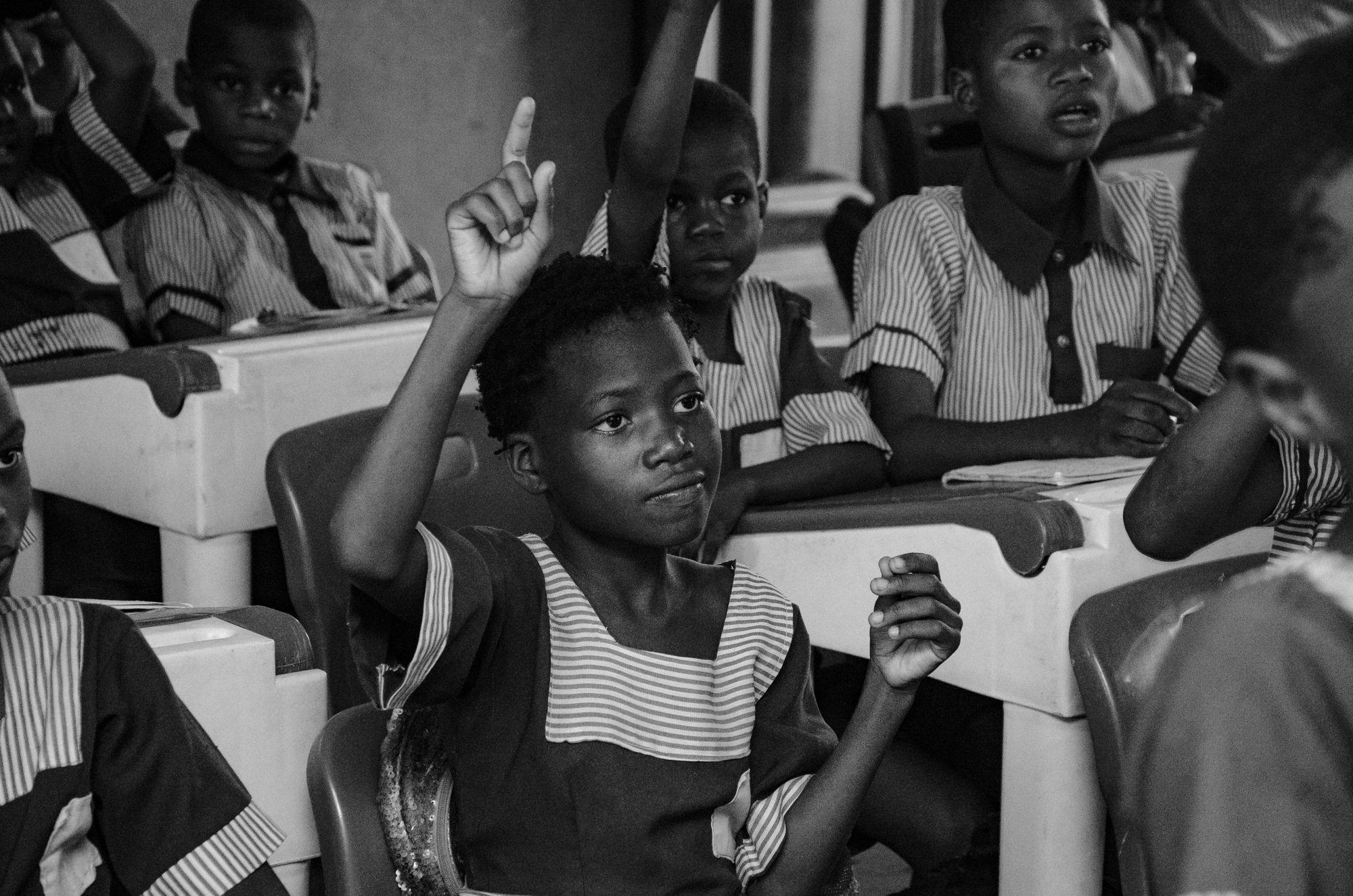 Pupils in a busy classroom raise their hands to answer a question.