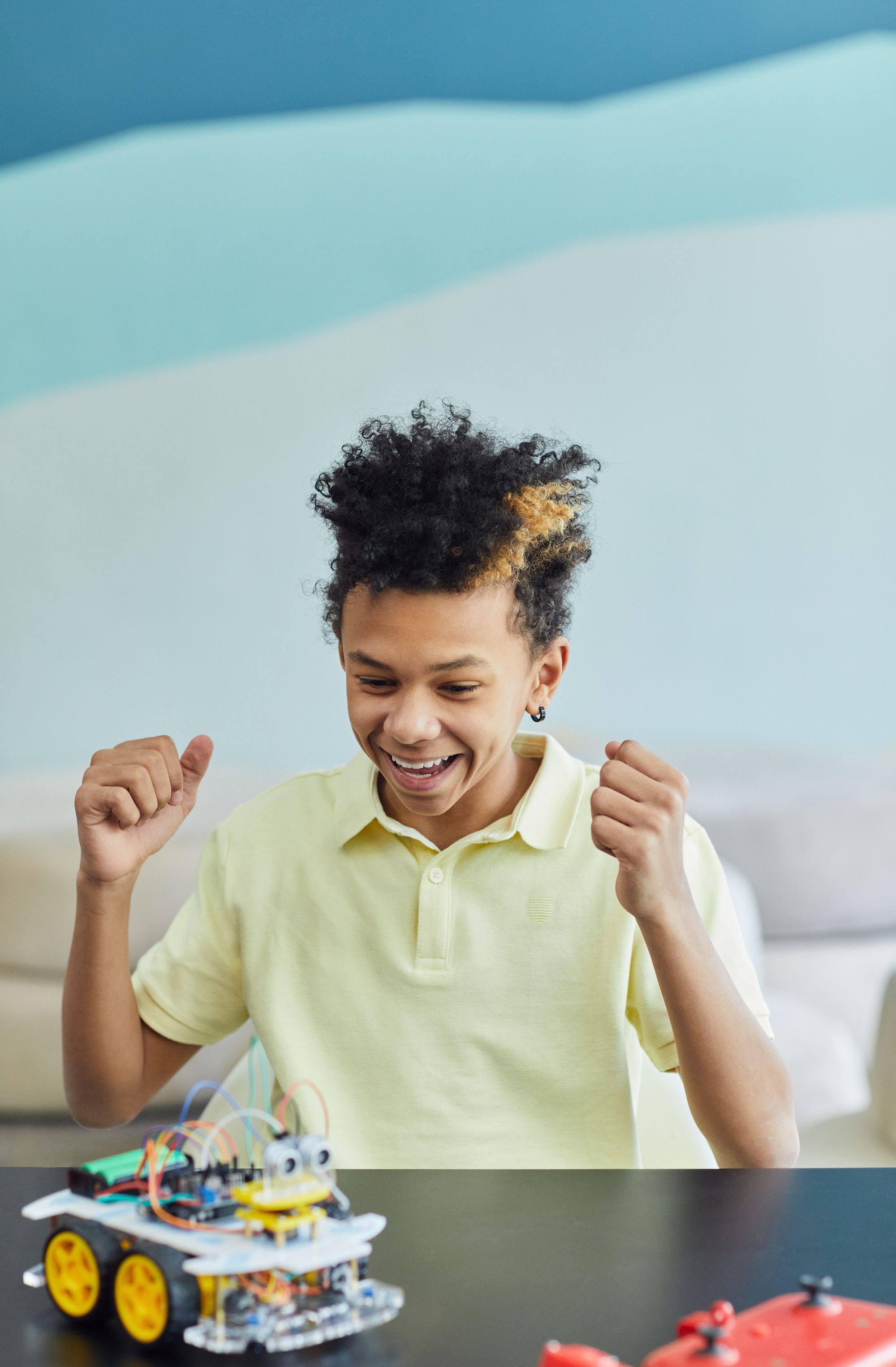 A boy cheers with both fists raised after his robot car works.