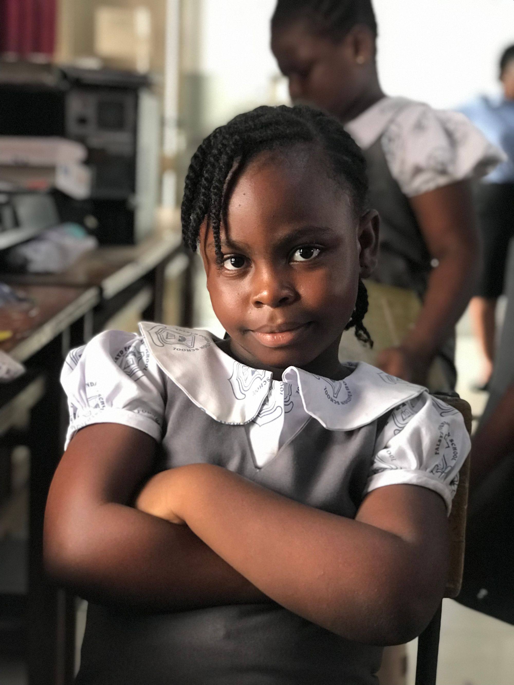 A confident schoolgirl stands with her arms crossed in a classroom in Ghana.