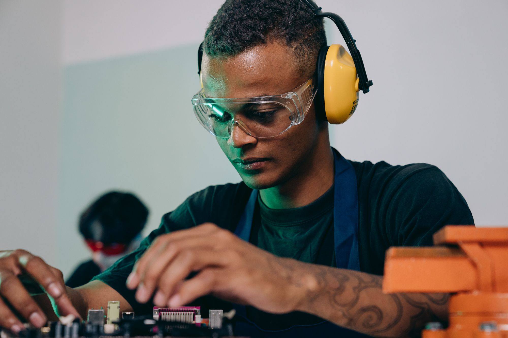 A young engineer in safety glasses and ear defenders solders a circuit board.