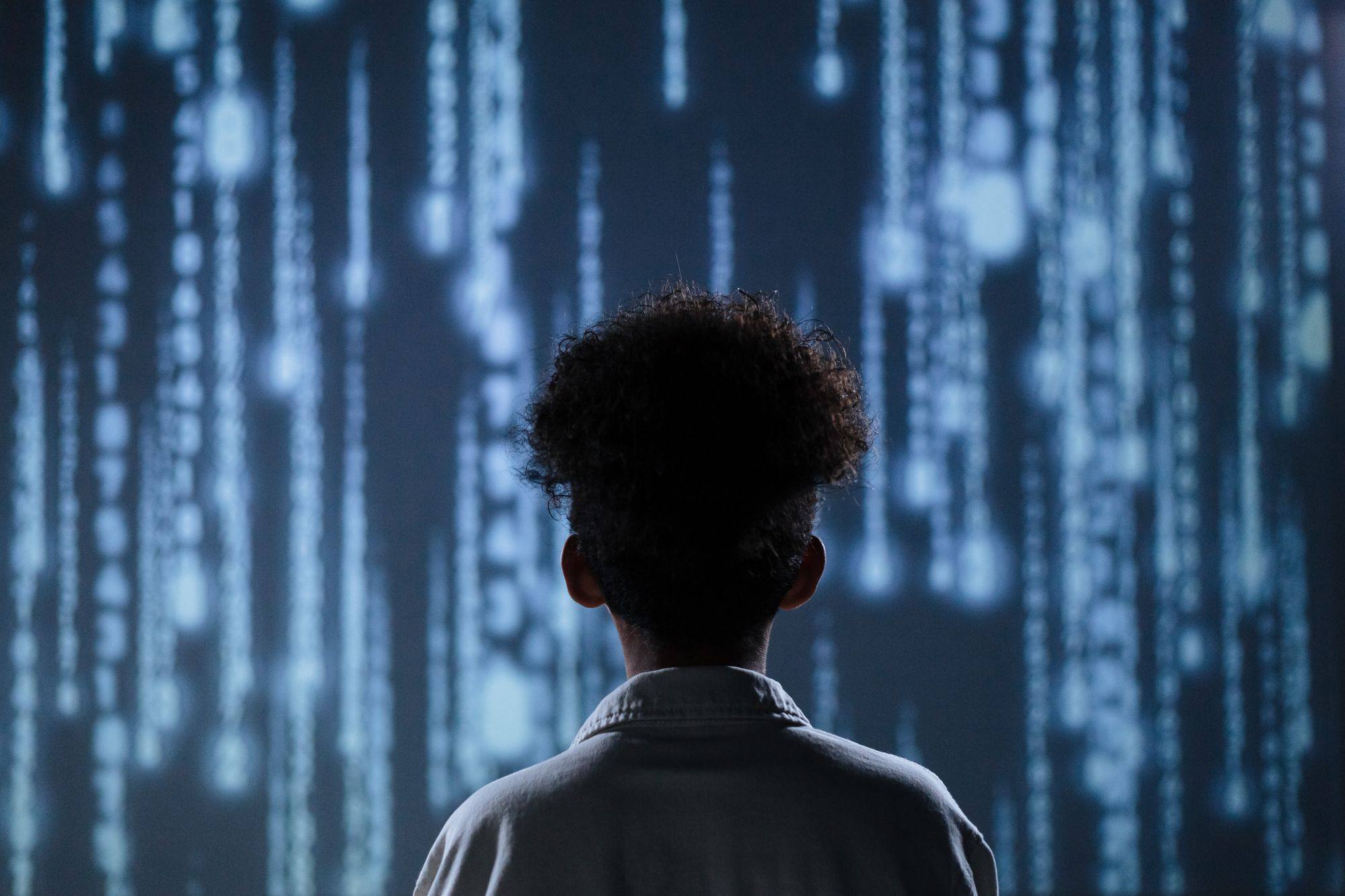 A child with curly hair, seen from behind, faces a wall of glowing data.