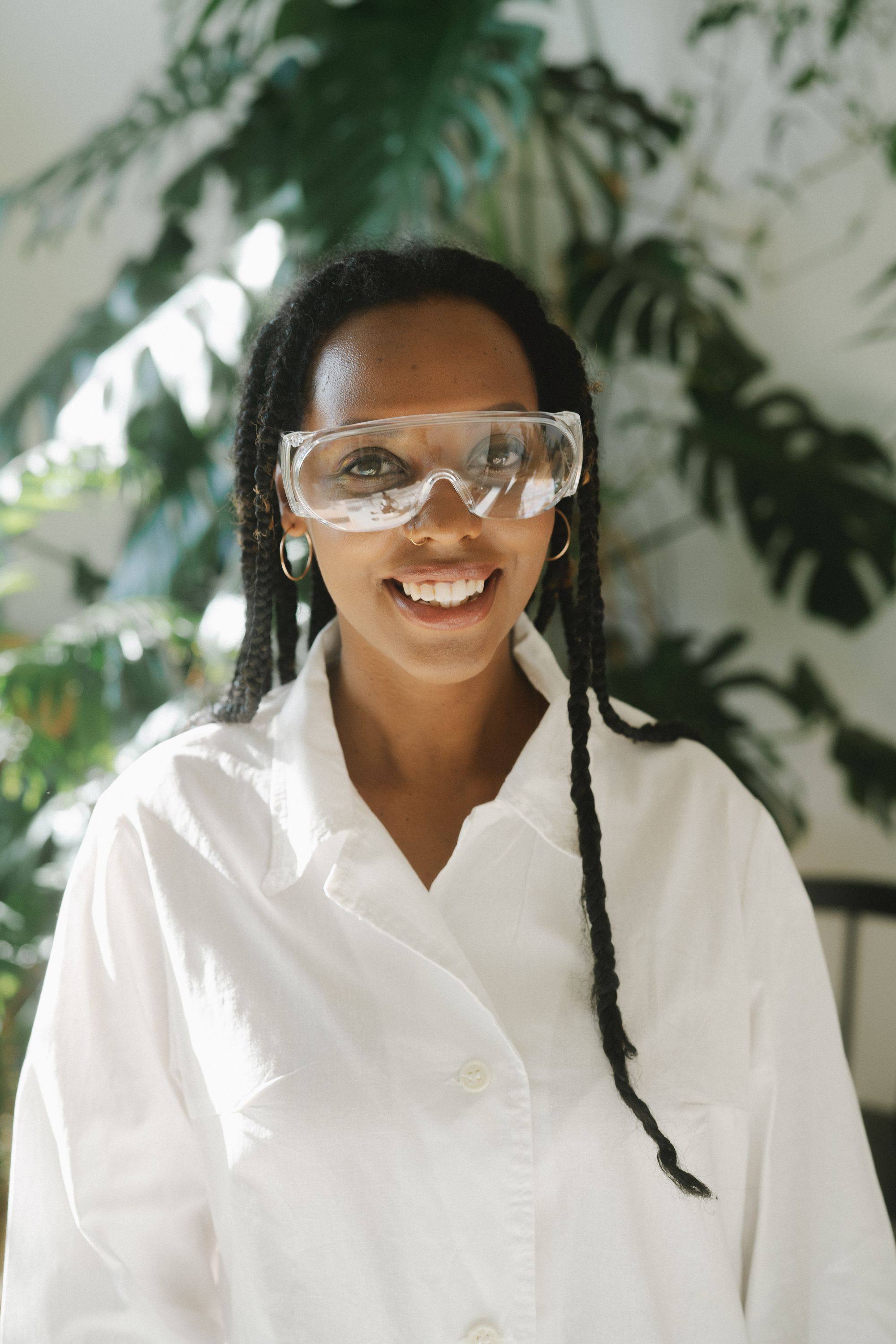 A smiling woman scientist wearing safety goggles and a lab coat.