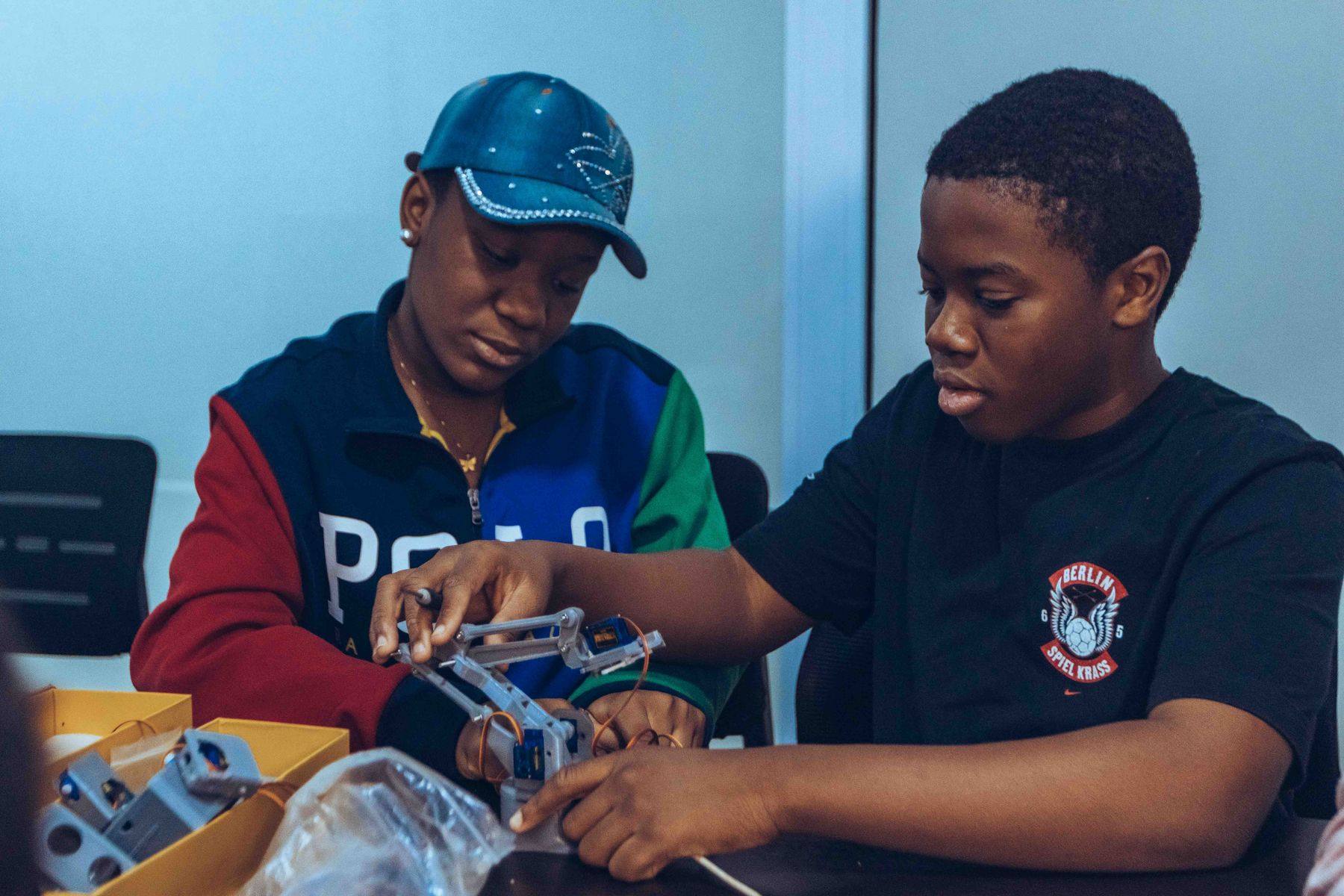 Two teenagers work side by side to assemble a mechanical arm at a workshop in Accra.