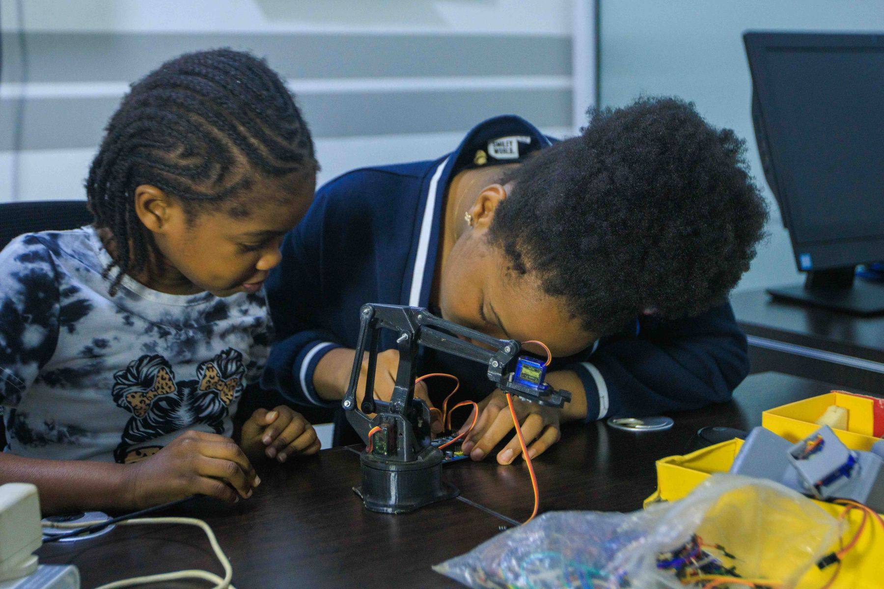 A girl and a boy lean in to build a small robot arm together at a workshop in Accra.